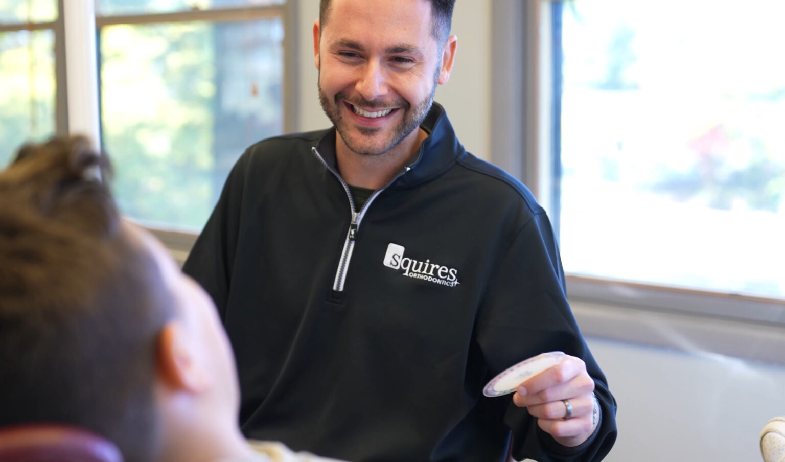 Orthodontist Dr. Squires laughing in his black Squires jacket while consulting with a patient