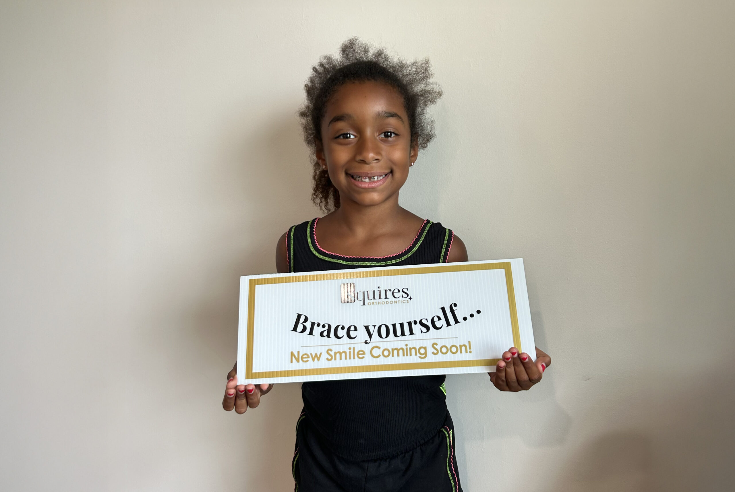 Squires Orthodontics child patient holding a sign showing that her smile is in progress