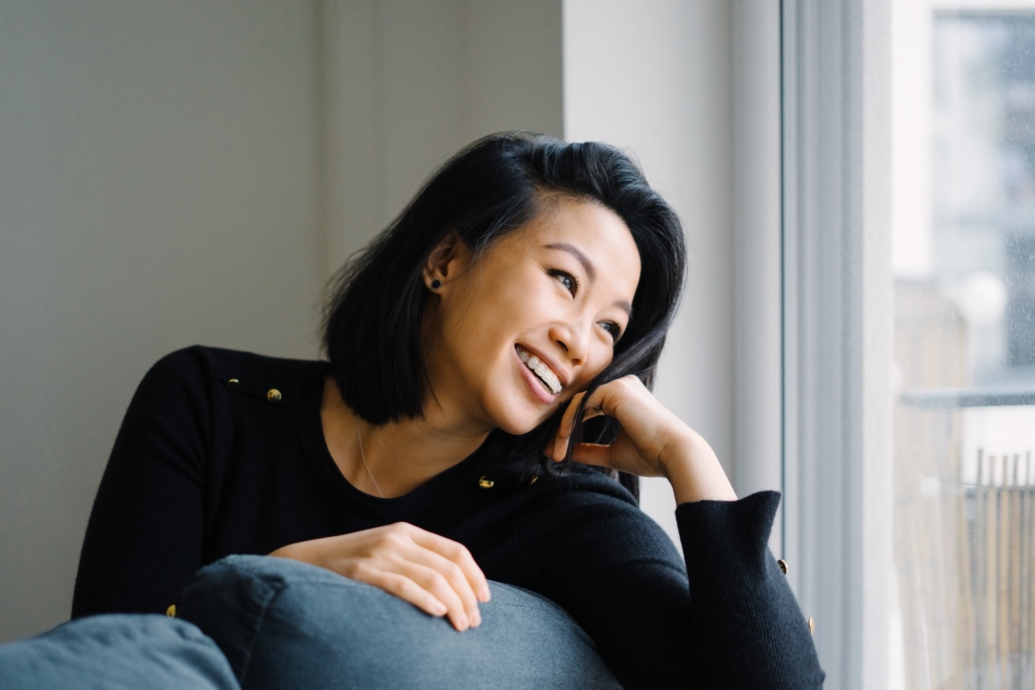 Woman with clear braces smiling and leaning over her couch to look out the window