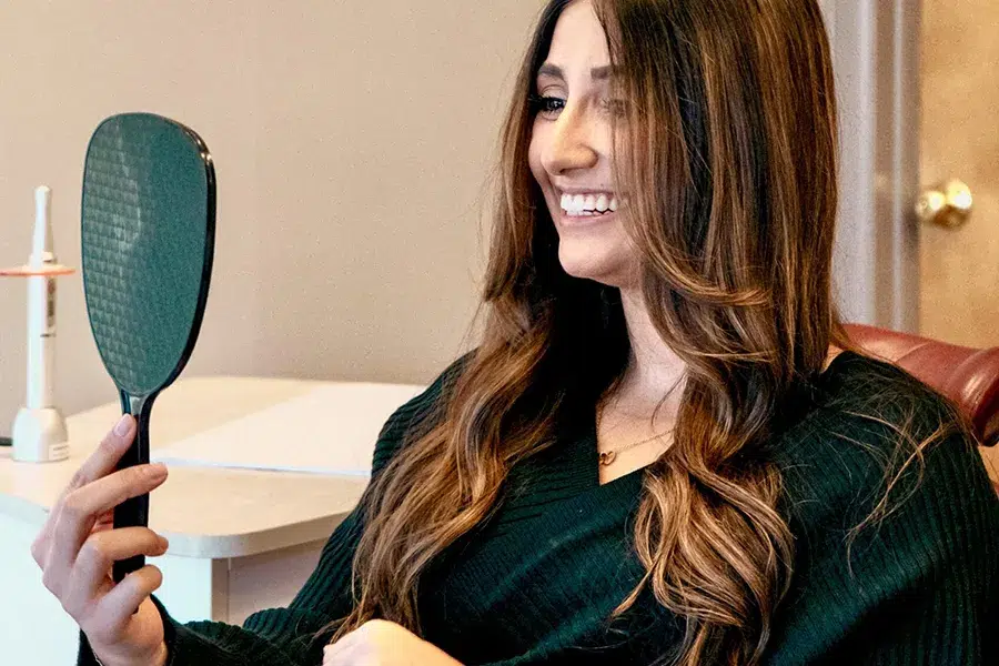 An orthodontist in a white doctor's coat holds up clear aligners to the camera